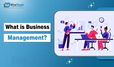 An illustrative graphic titled "What is Business Management?" featuring three professionals in an office setting. One person stands pointing at a presentation board with data charts, while two colleagues sit at a desk with laptops, collaborating in a modern workspace.